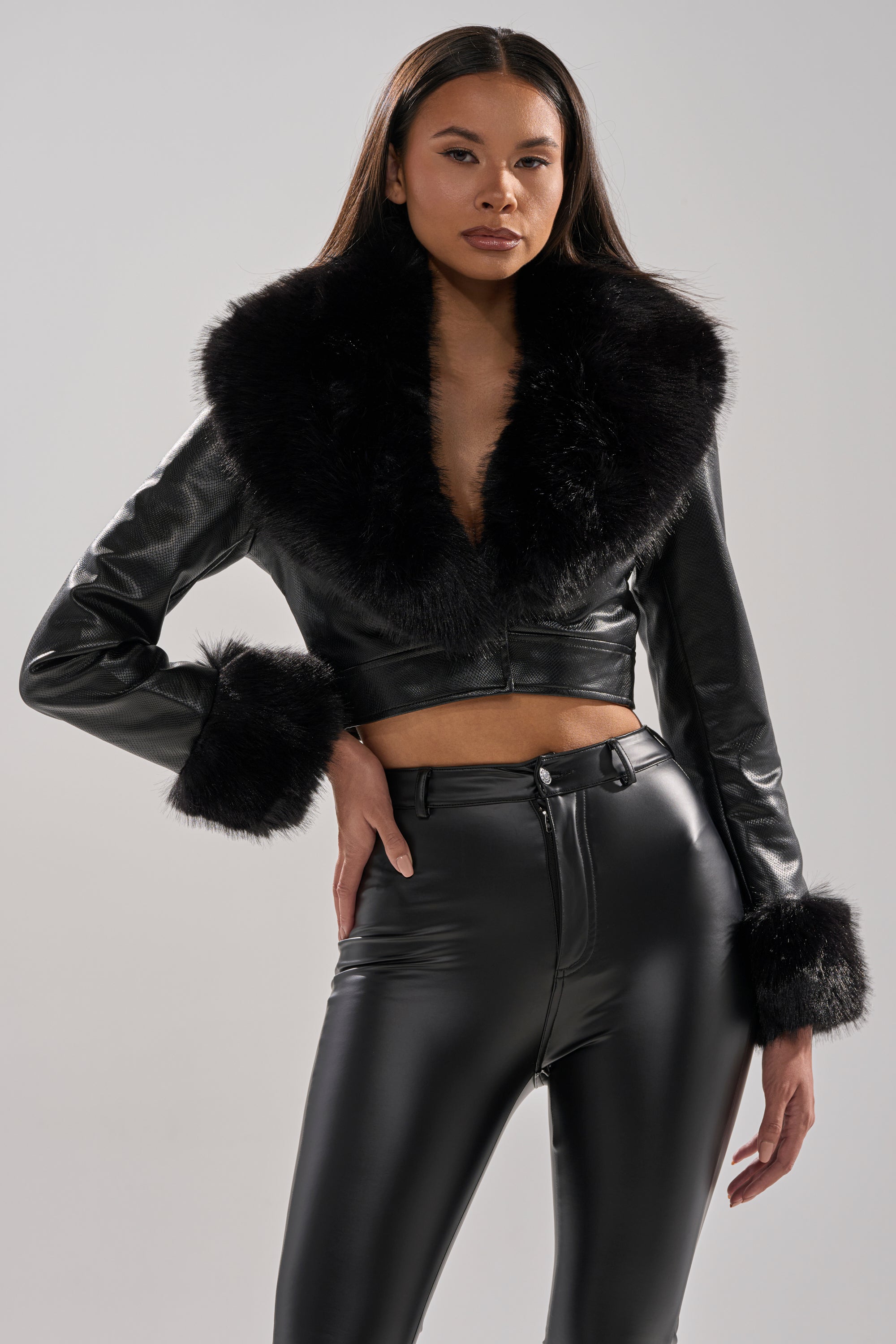 A woman exudes confidence against a light background, wearing the GISELE CROP MOTO BLAZER with a large faux fur collar and cuffs, paired with high-waisted black faux leather pants for a bold, edgy look.