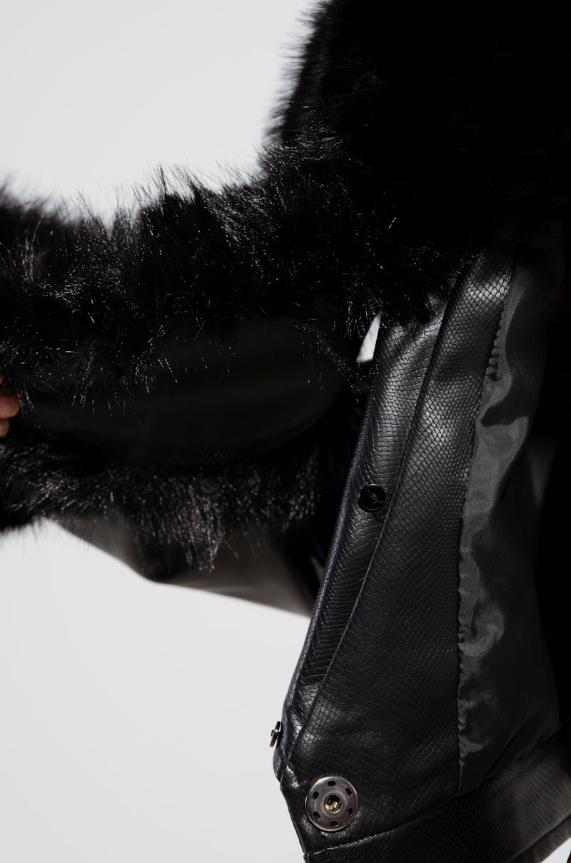 Close-up of a black fur-trimmed hood on the GISELE CROP MOTO BLAZER. The soft, fluffy detachable faux fur collar contrasts with the sleek croc-embossed faux leather material. A button and part of a zipper are visible on the blazer.