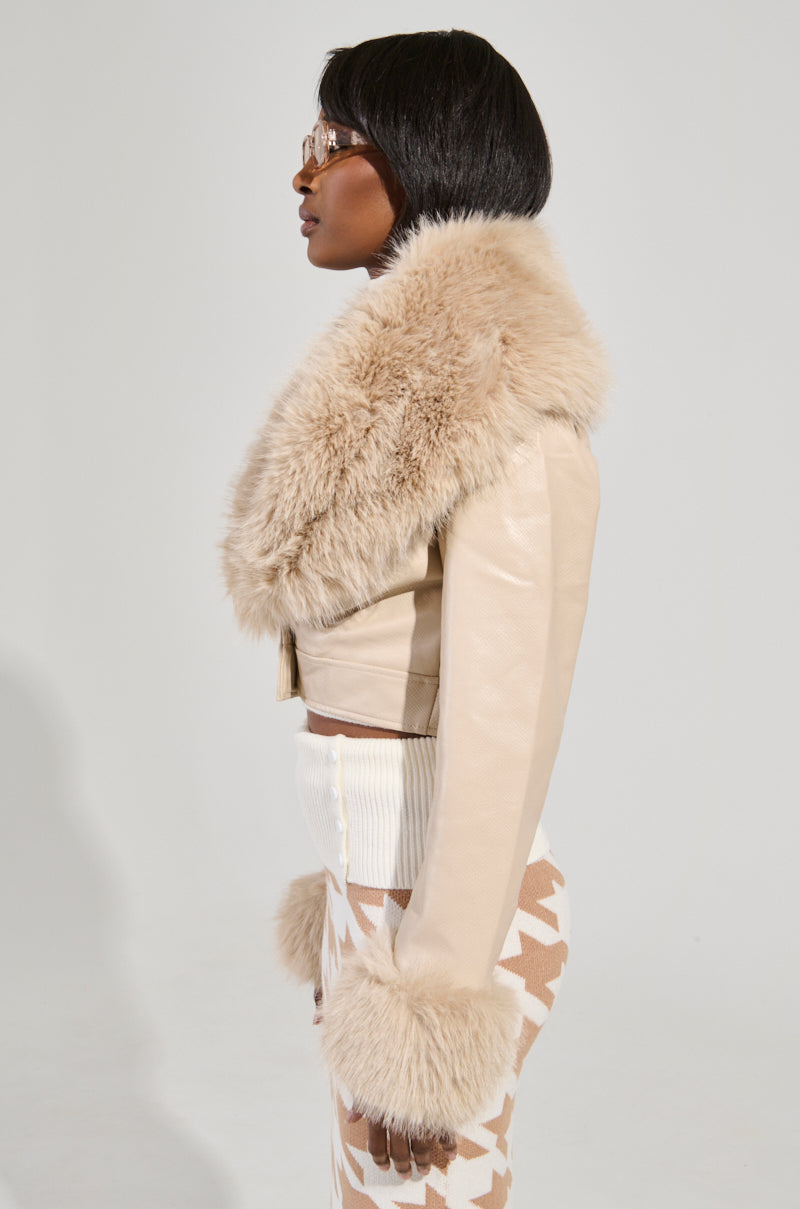 A person in profile wears a chic ensemble featuring an ivory Gisele Crop Faux Fur Moto Jacket, complete with removable faux fur trim and croc-embossed faux leather. Their look is finished with sunglasses, a white top, and patterned pants against a light-colored backdrop.