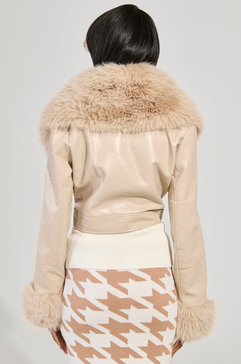The person is wearing a Gisele Crop Faux Fur Moto Jacket in ivory, showcasing a striking croc-embossed faux leather design. It features a large, removable faux fur trim collar and cuffs and is paired perfectly with a brown and white houndstooth skirt as they face away to highlight the back of the outfit.