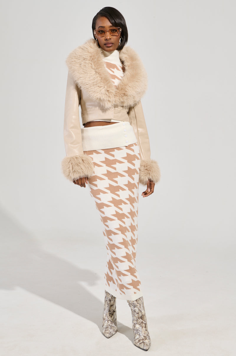 A person wearing the Gisele Crop Faux Fur Moto Jacket in ivory, featuring croc-embossed faux leather and a removable faux fur trim, paired with a beige and white houndstooth-patterned long skirt and snakeskin-patterned boots, stands confidently. Sunglasses complete the ensemble.