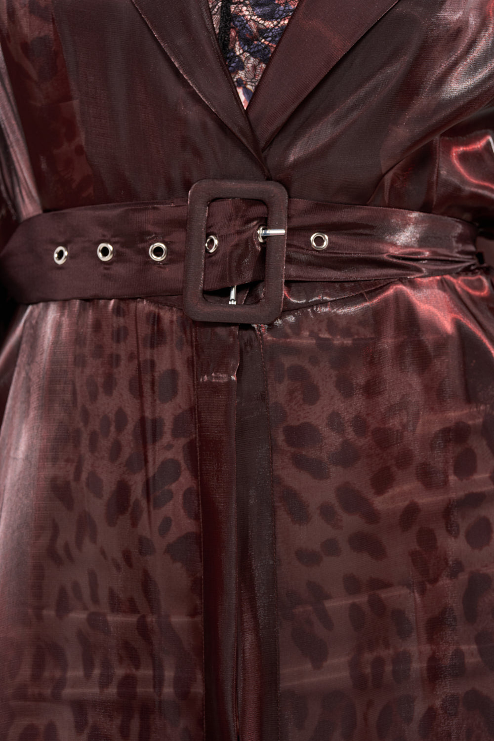 Close-up of the PRETTY LIL THING ORGANZA TRENCH: a shiny maroon belted trench coat with a matching square buckle, subtle animal print, and lace fabric peeking underneath. 8