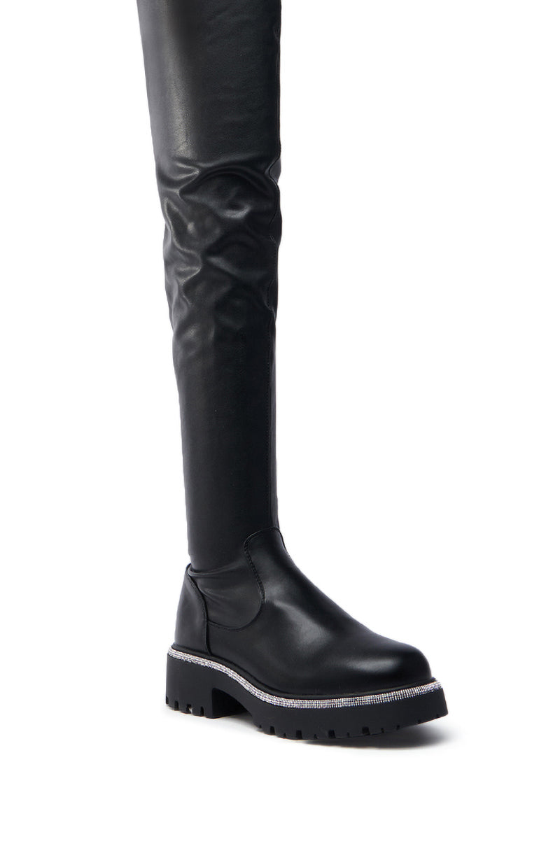 The AZALEA WANG NEWRULES RHINESTONE STRETCH PU FLAT BOOT is a black thigh-high boot with a shiny over-knee panel, chunky heel, and decorative rhinestone stretch trim, offering an eye-catching and fashionable design.