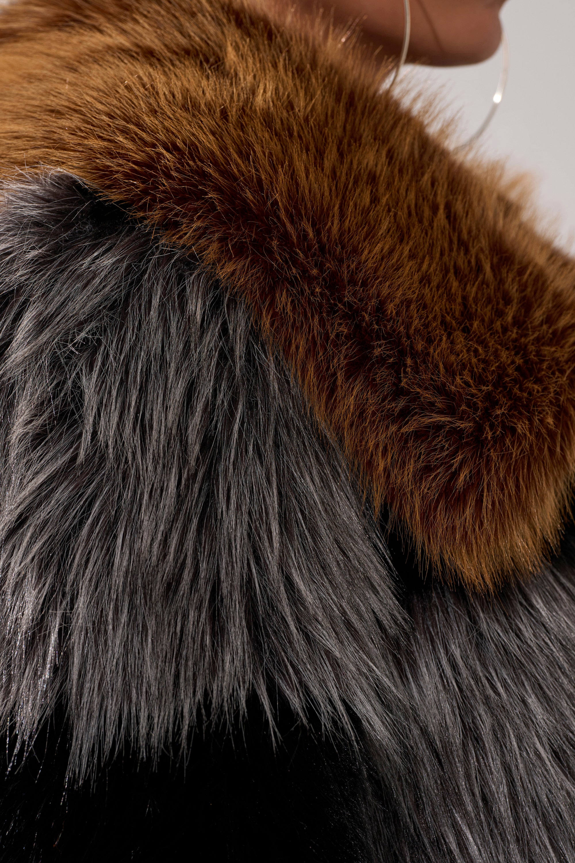 Close-up of a person wearing the HAZEL PATCHWORK FAUX FUR COAT, featuring a cropped fit with a brown collar and gray body that highlights the plush faux fur texture. Large hoop earring visible near the neck.