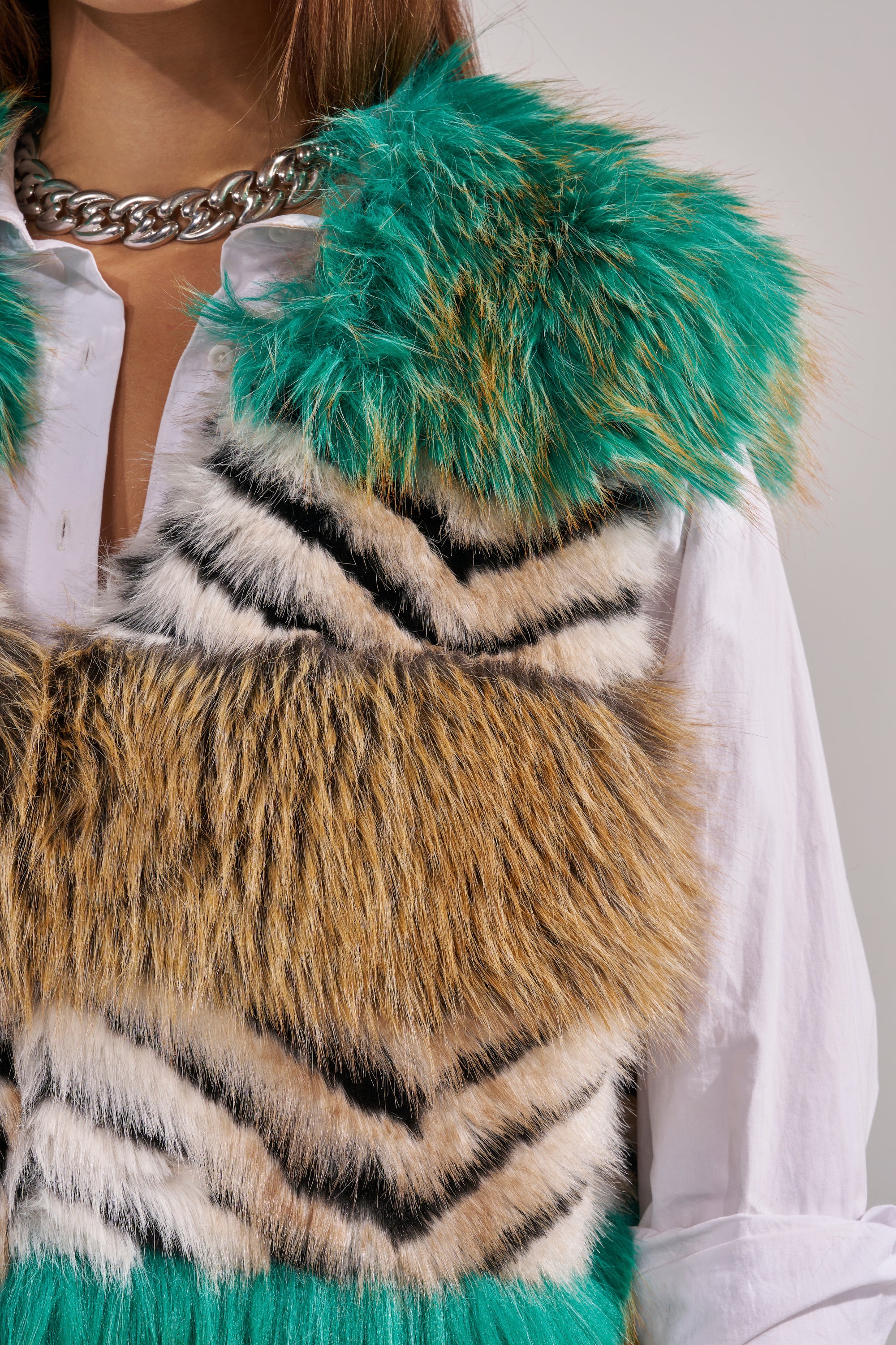 Wearing the HYDE PARK FAUX FUR VEST with green, brown, and black stripes over a white button-down and chunky silver chain necklace creates a look of winter luxury. 10