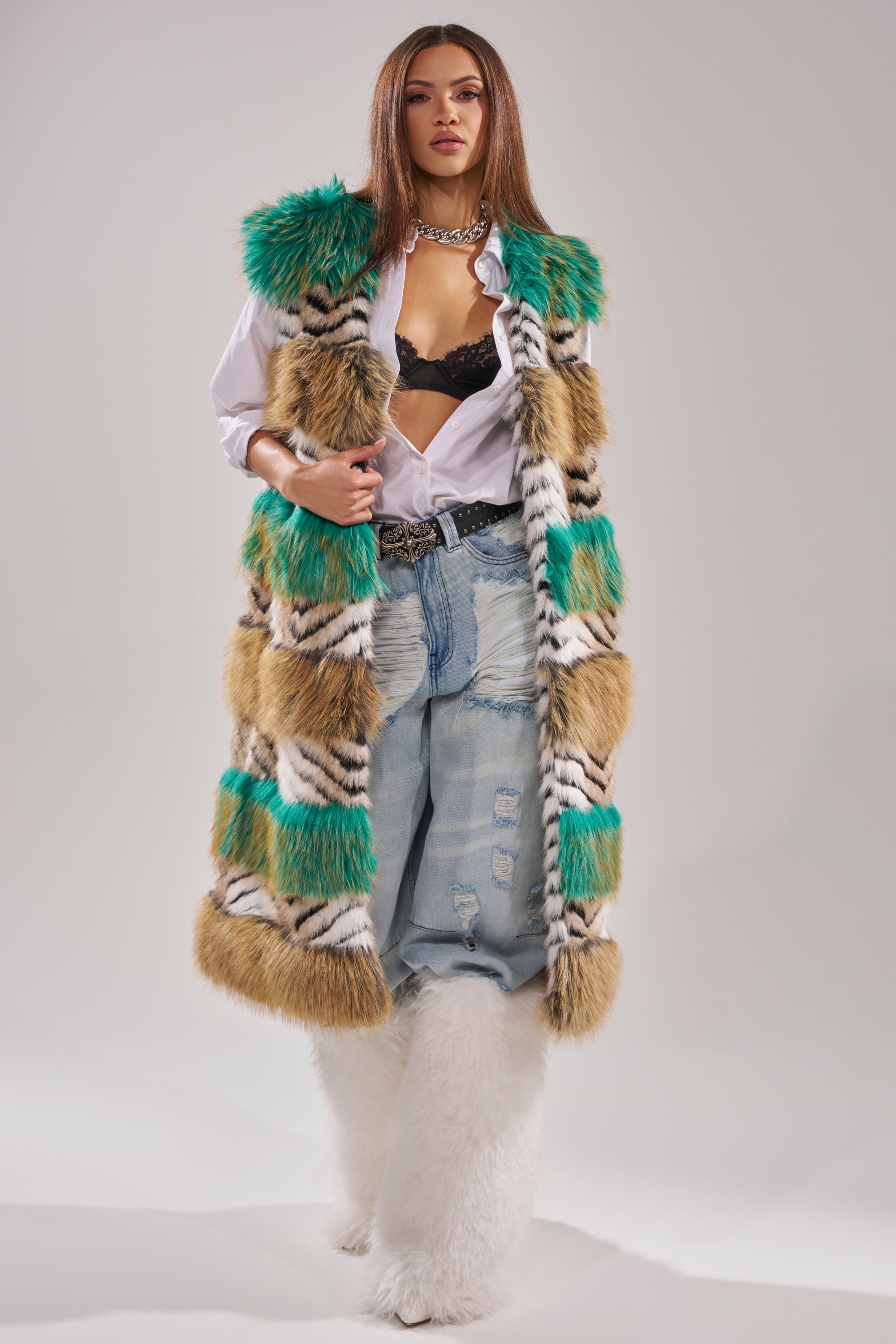 A woman stands confidently in the HYDE PARK FAUX FUR VEST, paired with a white shirt over a black lace bra, distressed baggy jeans, a chunky necklace, and large white furry boots—an effortless statement of winter luxury. 2