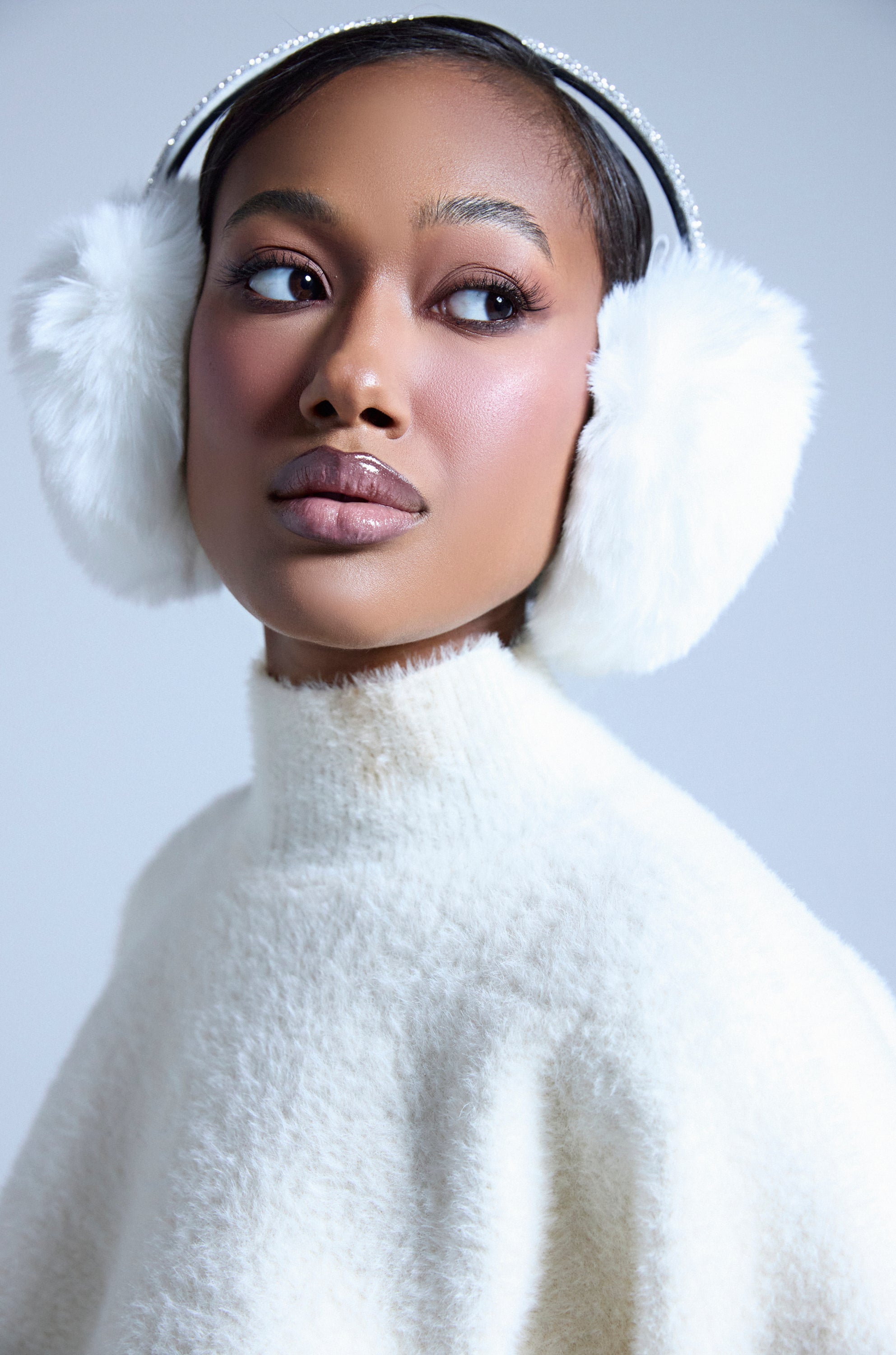 A woman showcases the EXTRA RHINESTONE EAR MUFFS IN WHITE and a white textured turtleneck, her sleek hair and natural makeup creating a polished winter look against a light background. 2