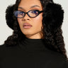 Wearing EXTRA RHINESTONE EAR MUFFS IN BLACK and cat-eye glasses with blue lenses, a person with long curly hair completes their winter look. My dressed in a sleek black top against a plain light background, they exude confidence while looking at the camera.