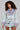 Sporting the AD ASTRA Fur Trim Jacket in light blue denim, a woman with curly hair channels Bratz-inspired fashion. The jacket's purple faux fur accents enhance her stylish look, while the accompanying skirt's metallic buckles and safety pins introduce an edgy flair. She completes her ensemble with a small chain strap purse.