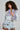 A woman with curly hair channels her inner Bratz by striking a pose against a plain backdrop while wearing the AD ASTRA FUR TRIM JACKET IN LIGHT BLUE DENIM, featuring a purple fur collar and cuffs, paired with a denim mini skirt adorned with multiple buckles.