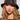 A person with long, wavy hair wears the WITH LOVE PATCH BUCKET HAT, which features beaded designs and embroidered patches, including a prominent face motif. They have a serious expression and are dressed in a sheer, embellished top.