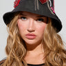A person with long, wavy hair wears the WITH LOVE PATCH BUCKET HAT, which features beaded designs and embroidered patches, including a prominent face motif. They have a serious expression and are dressed in a sheer, embellished top.