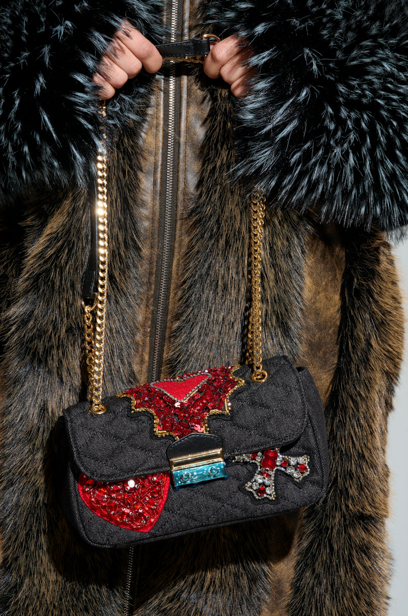 A person wearing a fur coat holds the REGIS PATCHWORK QUILTED PURSE, which features red and silver sequin embellishments, an elegant gold chain strap, and intricate embroidered patches.