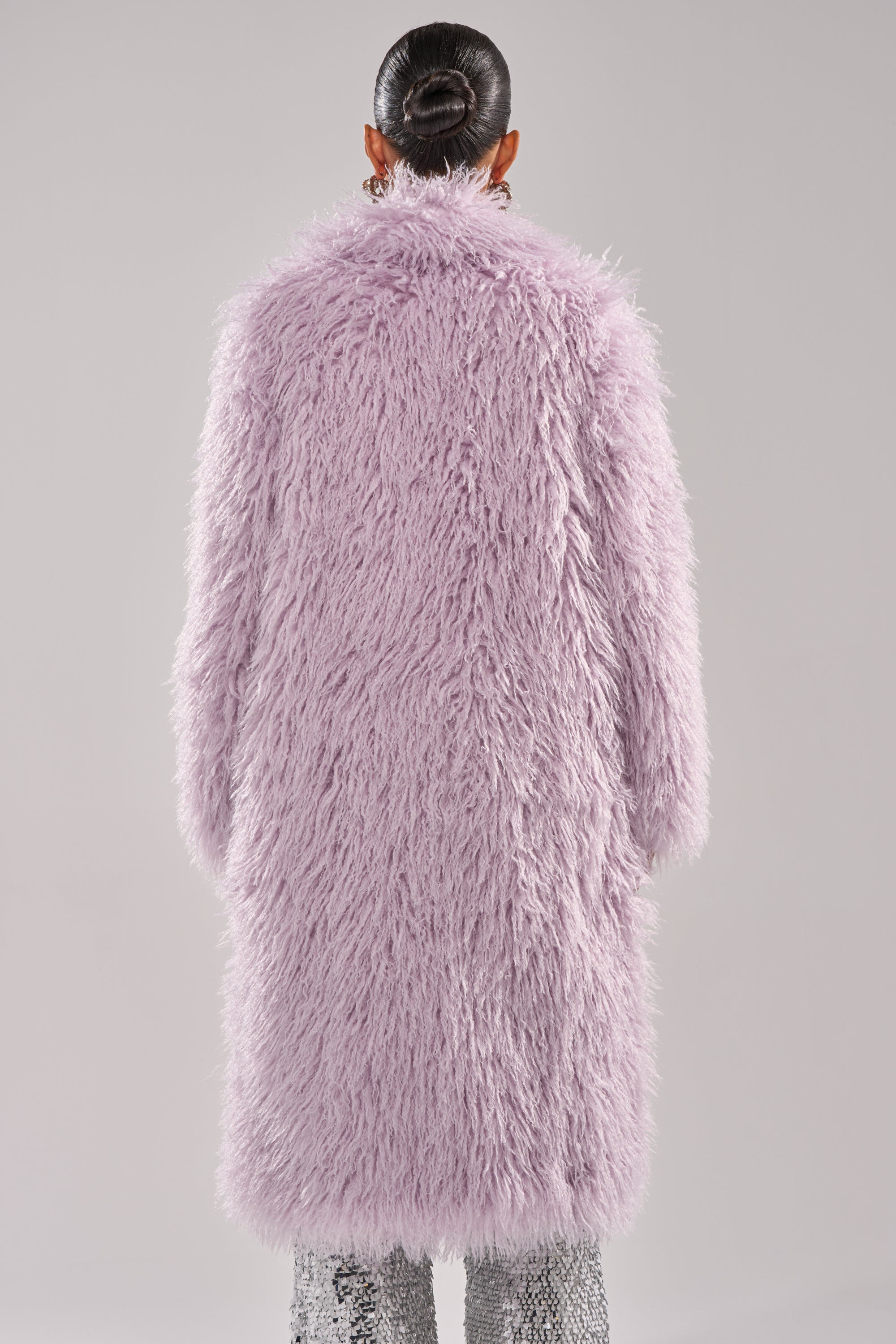 A person with hair in a sleek bun is shown from the back, wearing the VIOLET SKIES FAUX FUR COAT in lavender and sparkly silver pants against a plain background. 5
