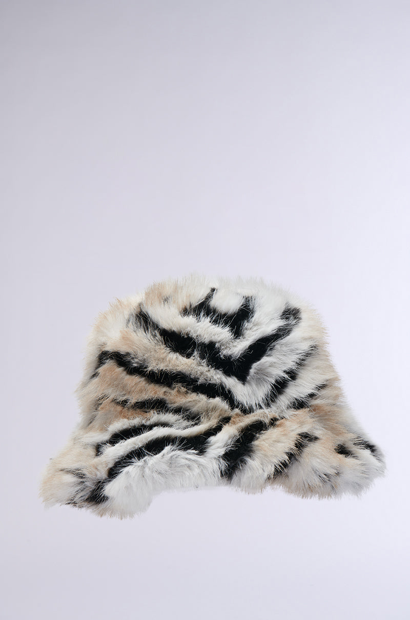 The WILDER FAUX FUR BUCKET HAT features a soft, plush appearance with its fuzzy black-and-white zebra pattern and a subtle brown tinge, set against a simple light gray background. 3
