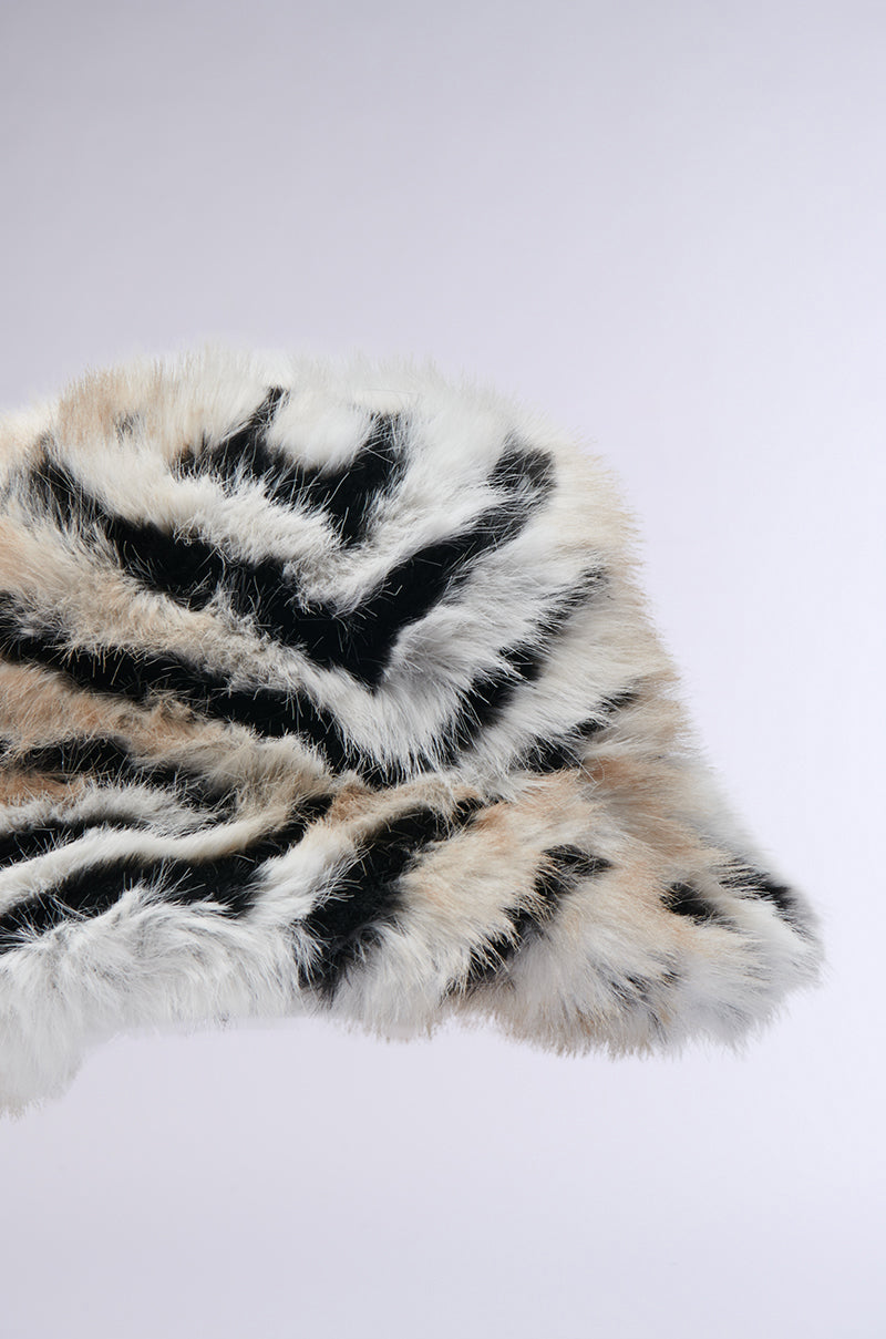 The WILDER FAUX FUR BUCKET HAT features a zebra-inspired black and white striped pattern, offering a soft, cozy texture that looks both warm and stylish against a plain background. 4