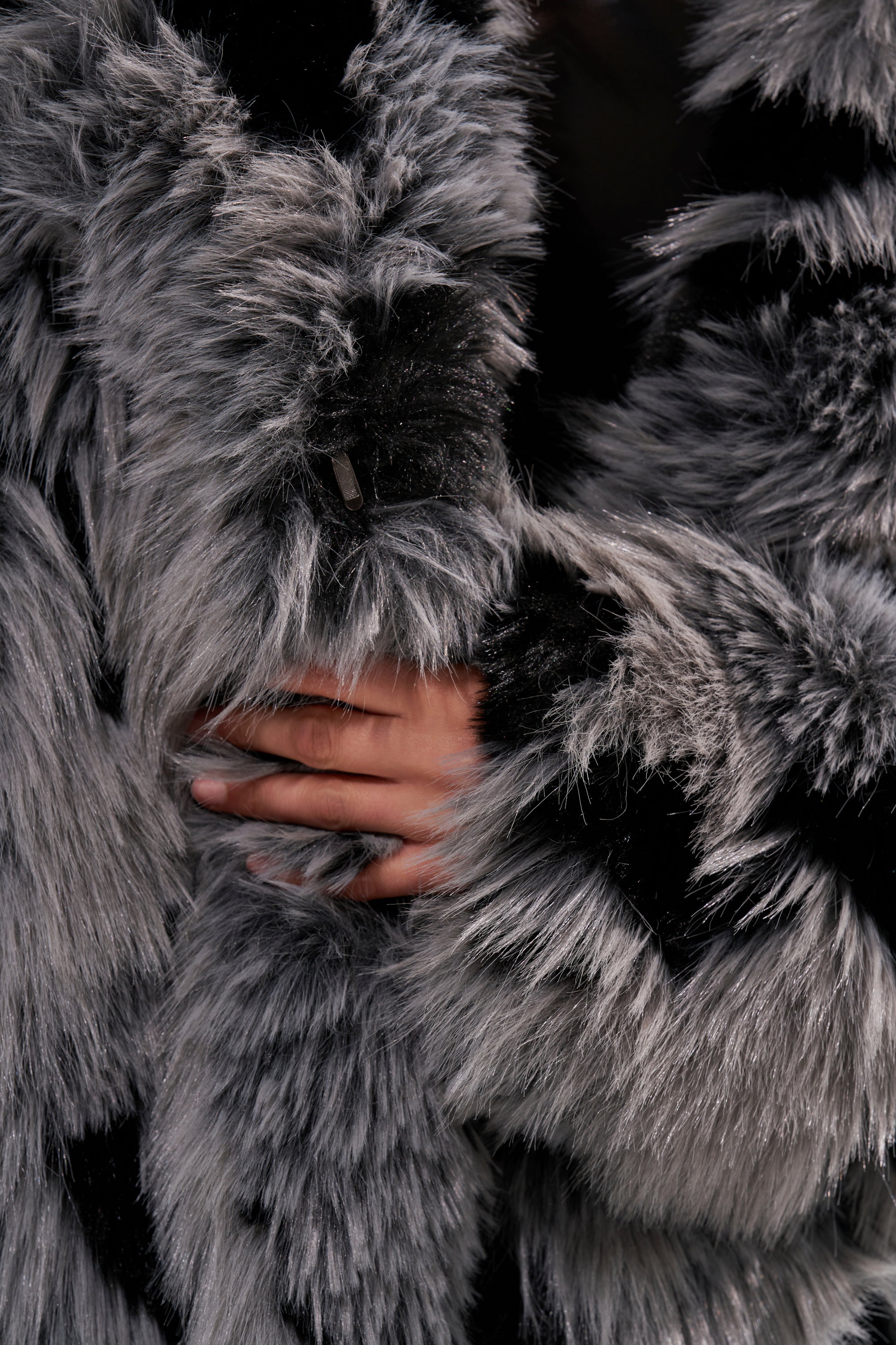A hand rests on the APRES SKI FAUX FUR COAT, showcasing its fluffy gray and black faux fur texture—soft, thick, and ideal for a cozy longline silhouette after a day on the slopes.