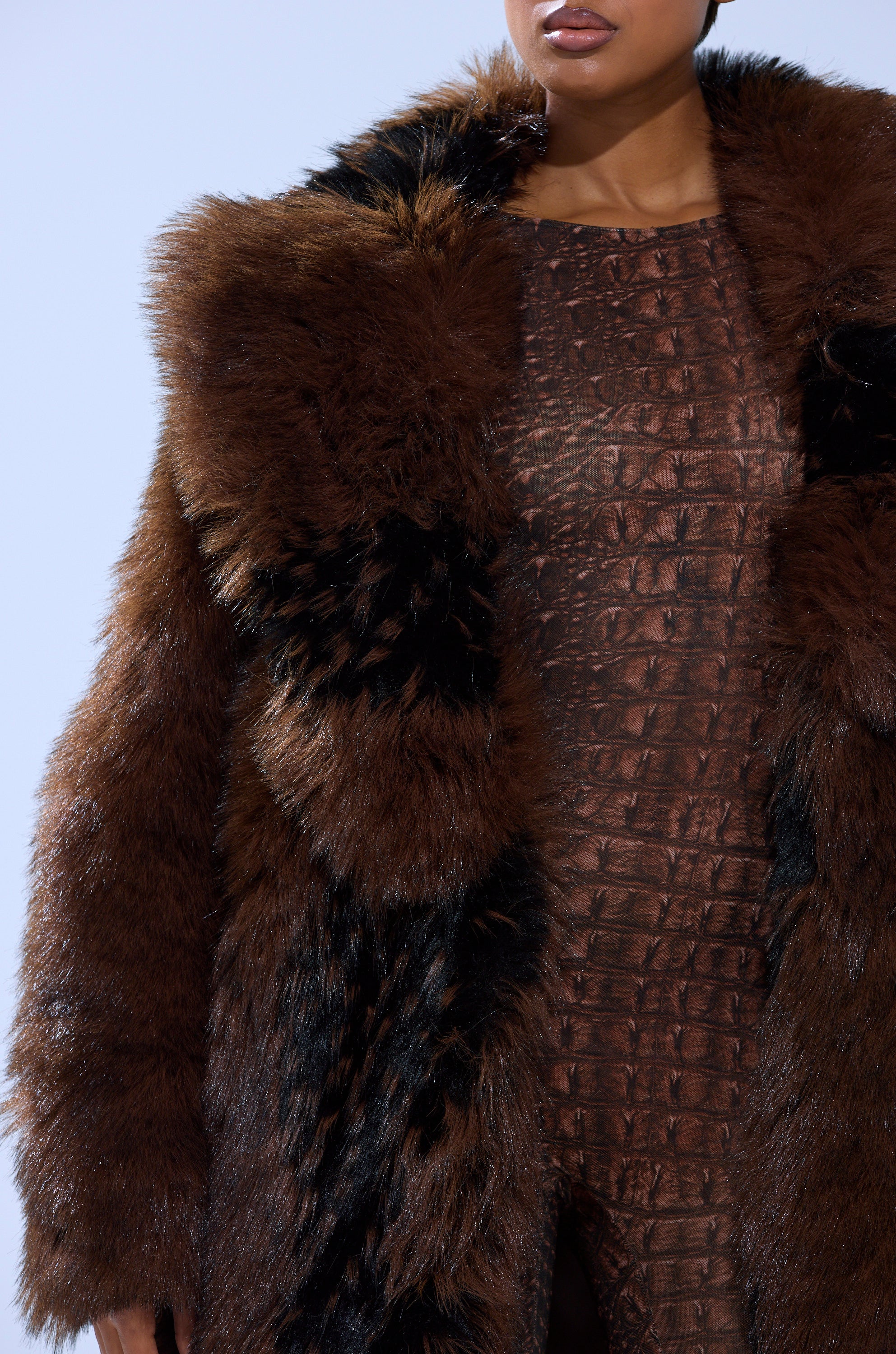 Wearing the Telluride Faux Fur in Brown, a dark brown jacket with an oversized collar and black accents, styled over a textured, crocodile-patterned brown outfit and shown from the shoulders to the thighs.
