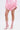 A person in a light pink ruffled mini skirt, matching tailored jacket, and AZALEA WANG NICKLAS PINK LEOPARD STILETTO BOOTIE stands against a plain white background. Their head is not visible in the image.