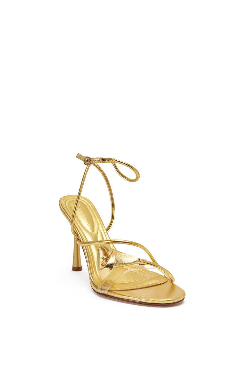 The AZALEA WANG NILO GOLD METALLIC FLORAL DECALE STRAP STILETTO SANDAL features thin metallic gold straps, a stiletto heel, and a bow-tied ankle strap, displayed on a plain white background. 4