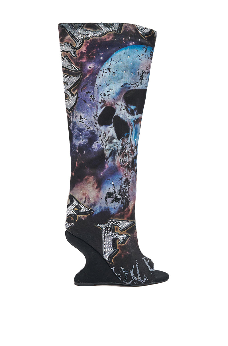 The AKIRA GOLD NINE LIVES GRAPHIC OPEN TOE WEDGE BOOT is a tall, knee-high wedge featuring a large blue skull, space-inspired graphics, bold textured lettering, an open rounded toe, sculpted heel, and eye-catching rhinestone details.