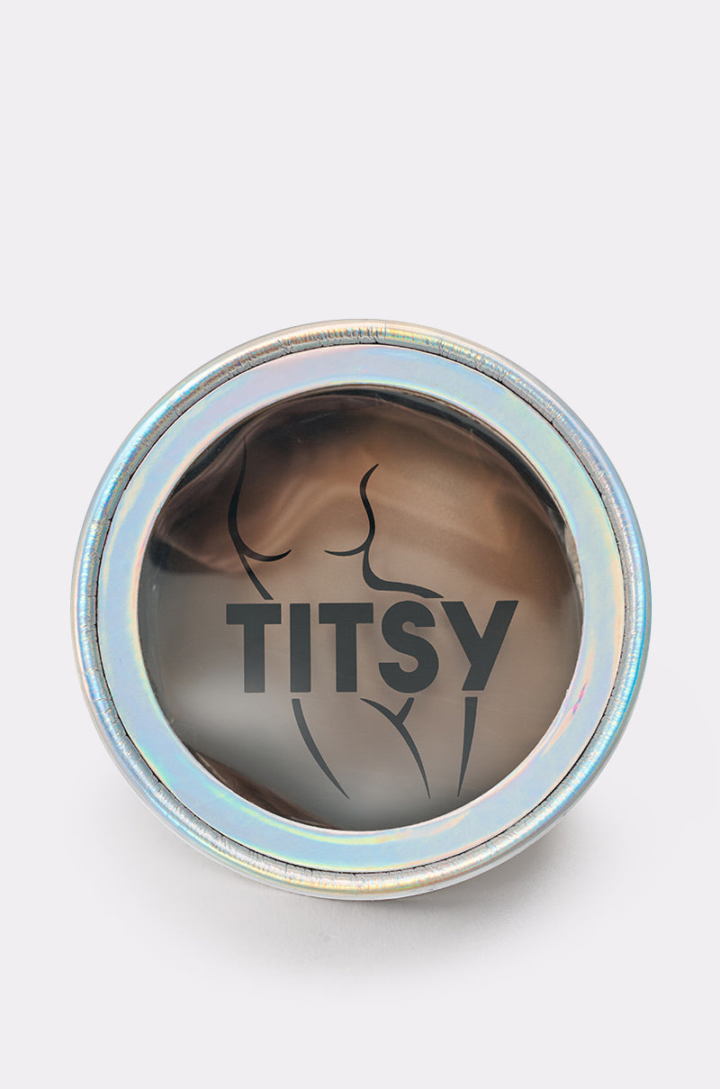 A round metallic tin with a shiny, iridescent lid displays "TITSY" and an abstract woman's outline—perfect for storing your TITSY ADHESIVE SILICONE NIPPIE PETAL. 1
