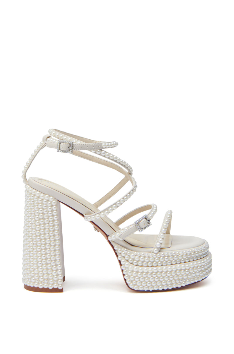 The AZALEA WANG NIYA IVORY PEARL SANDAL features faux leather straps, a chunky heel, silver buckles, small pearl bead accents, and a chic peep-toe design for an elegant look.