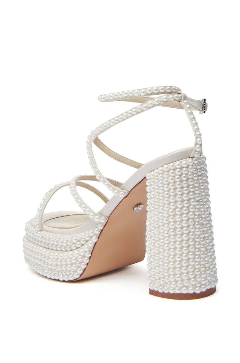 The AZALEA WANG NIYA IVORY PEARL SANDAL showcases a chunky heel, platform, crisscross straps with ankle buckle, white pearl embellishments, faux leather upper, and a light brown sole for an elegant touch.