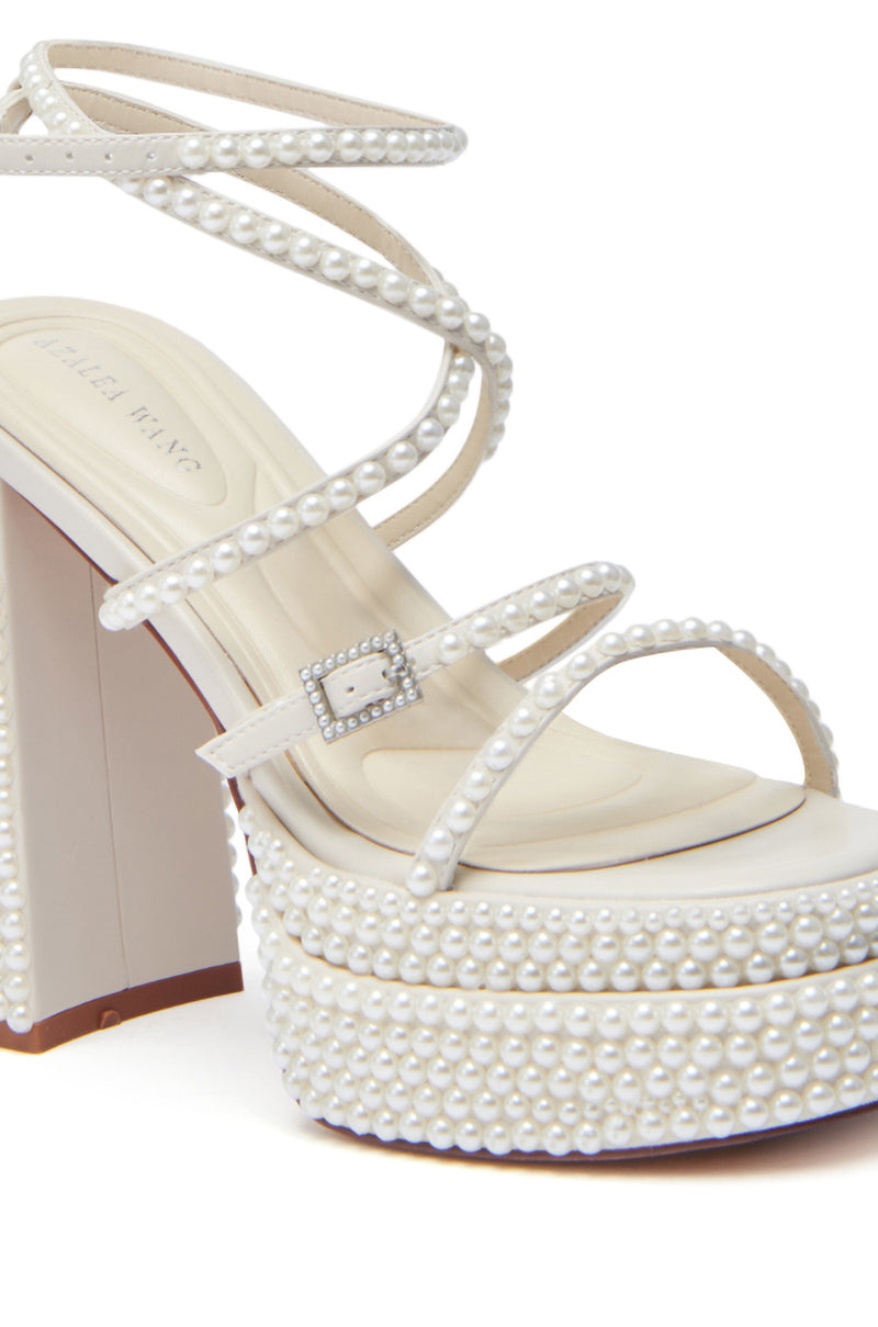 The AZALEA WANG NIYA IVORY PEARL SANDAL showcases multiple faux leather, pearl-embellished straps, a pearl-detailed buckle, and a chunky white pearl-covered heel and sole for a sophisticated look.