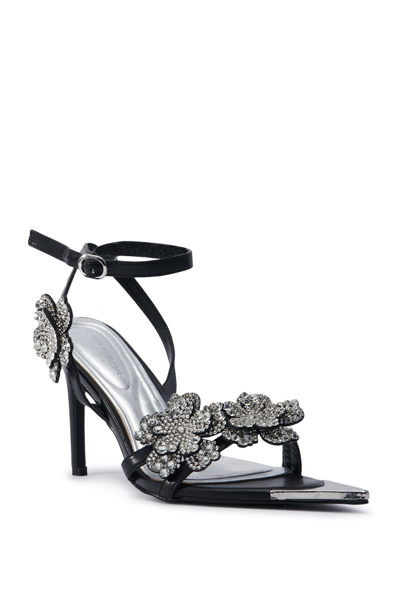 The AZALEA WANG NJEMA FLOWER EMBELLISHED STILETTO SANDAL is a black high-heeled shoe featuring a thin ankle strap, adorned with rhinestone floral appliques on the toe strap and side. It offers a sleek, elegant design with a pointed open toe.