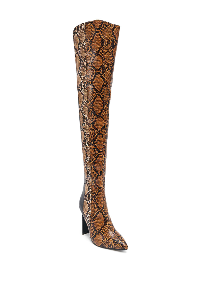 The AKIRA GOLD NOAMI MULTI SNAKE PRINT CHUNKY HEEL BOOT is a single knee-high, pointed-toe faux leather boot with a brown and black snakeskin pattern, chunky block heel, and sleek silhouette shown against a white background.