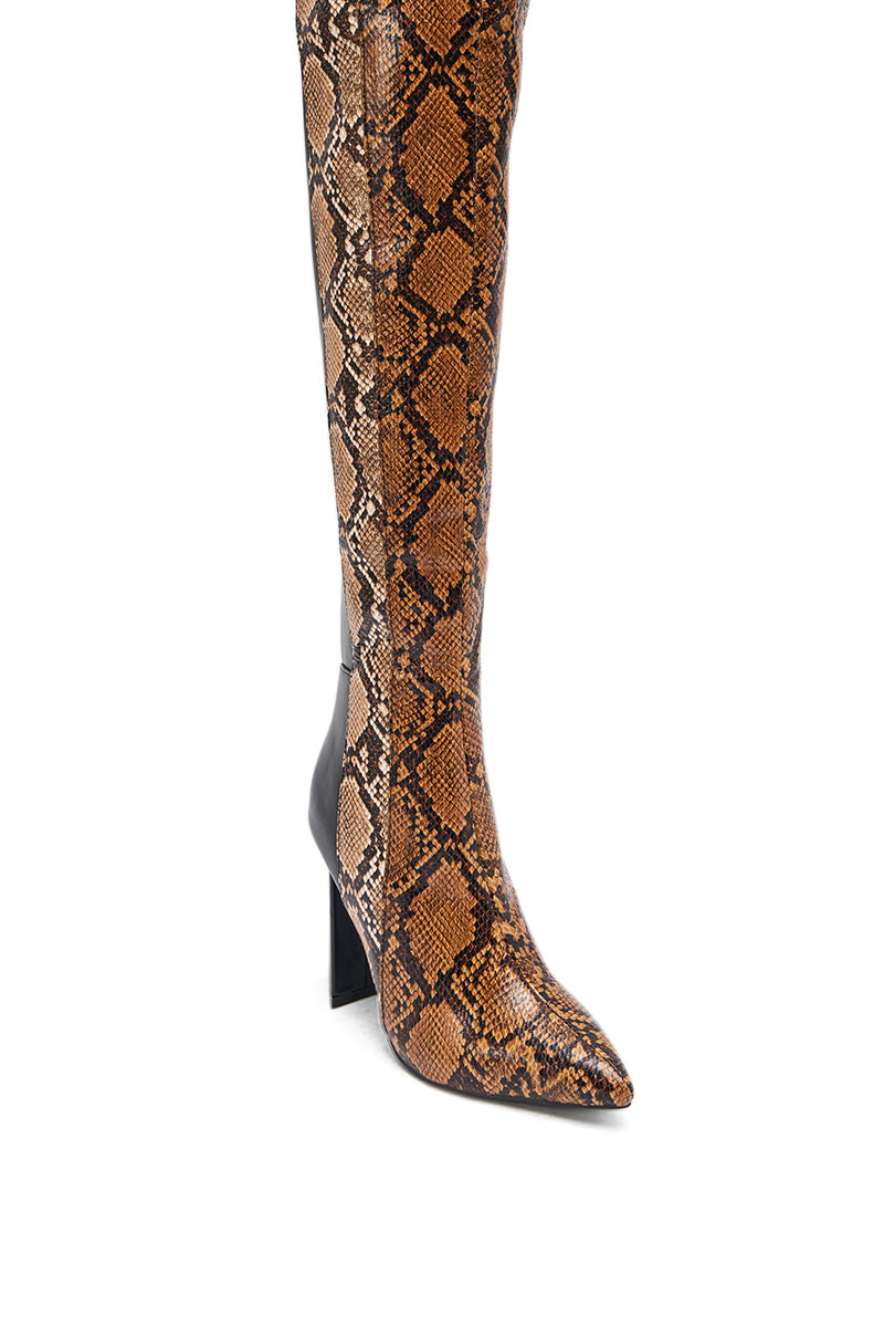The AKIRA GOLD NOAMI MULTI SNAKE PRINT CHUNKY HEEL BOOT features brown and black faux leather with a snakeskin pattern, pointed toe, and chunky high heel, displayed against a white background.