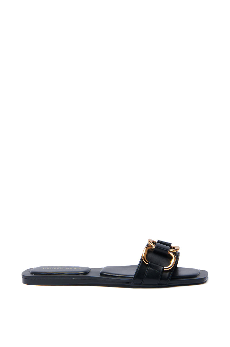The AKIRA NOELINE Black Slip-On Sandal features a flat sole and wide strap with a large gold-tone buckle, set against a plain white background to highlight the chic gold hardware detailing.