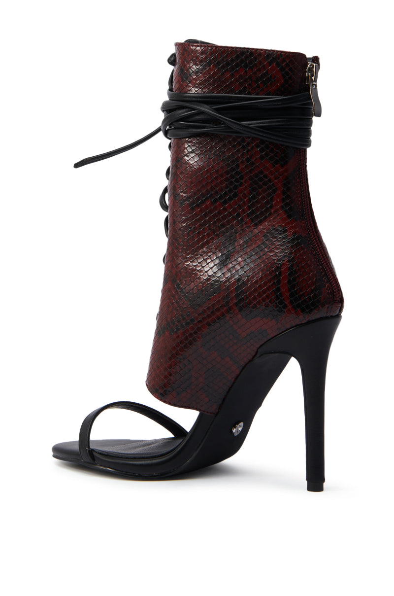 The AZALEA WANG NOLYN BURGUNDY SNAKE OPEN TOE BOOTIE features a red and black faux snakeskin upper, stiletto heel, open toe, thin black ankle strap, lace-up front, and a back zipper—perfect for making a bold statement. 4