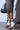 Wearing black and white stiletto-heeled lace-up boots with cropped denim, they stand on concrete, holding a sleek black faux leather handbag. Shadows dance intriguingly on the wall behind. (AZALEA WANG NOLYN HEELED SANDAL).
