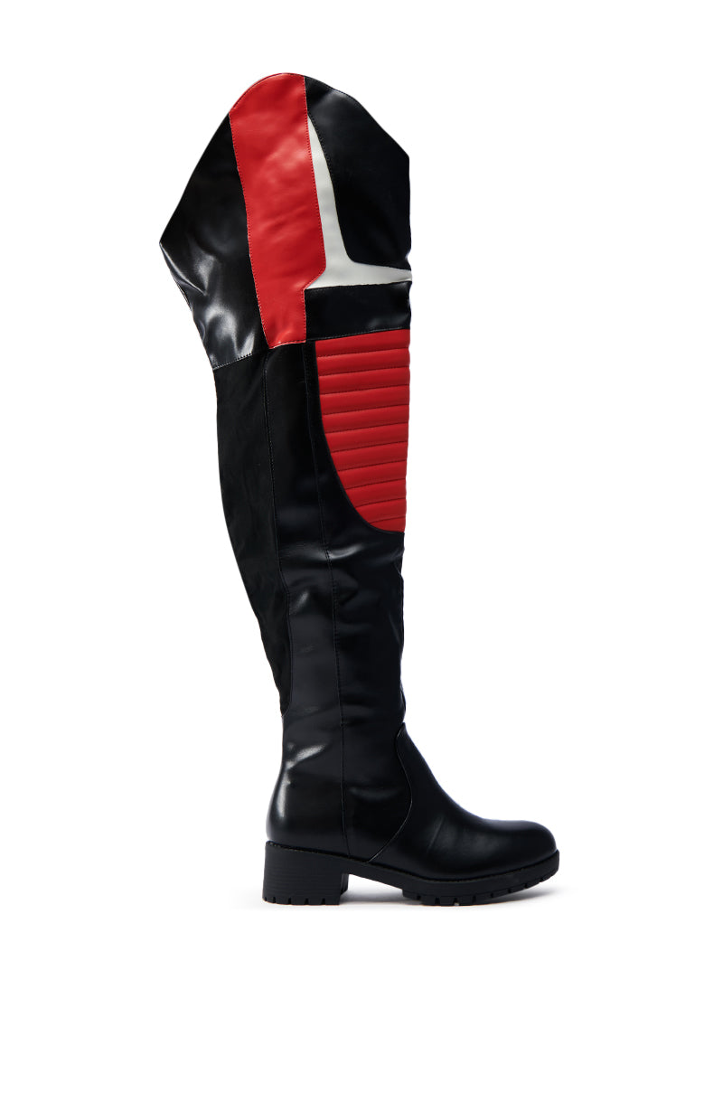 The NORRIS RED AND BLACK FLAT BOOT is a knee-high faux leather boot with a chunky rubber lug sole and bold red and white geometric design. It has a raised front section and is shown against a plain white background.