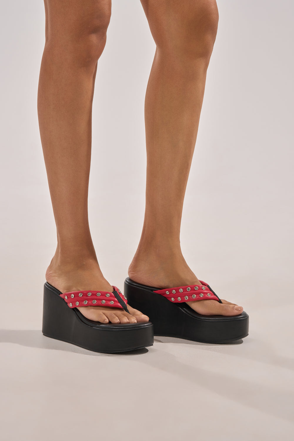 A person wearing AZALEA WANG NOVELLE BLACK AND RED STUD EMBELLISHED PLATFORM SANDALS stands on a light-colored surface, with only their lower legs and feet visible. 2