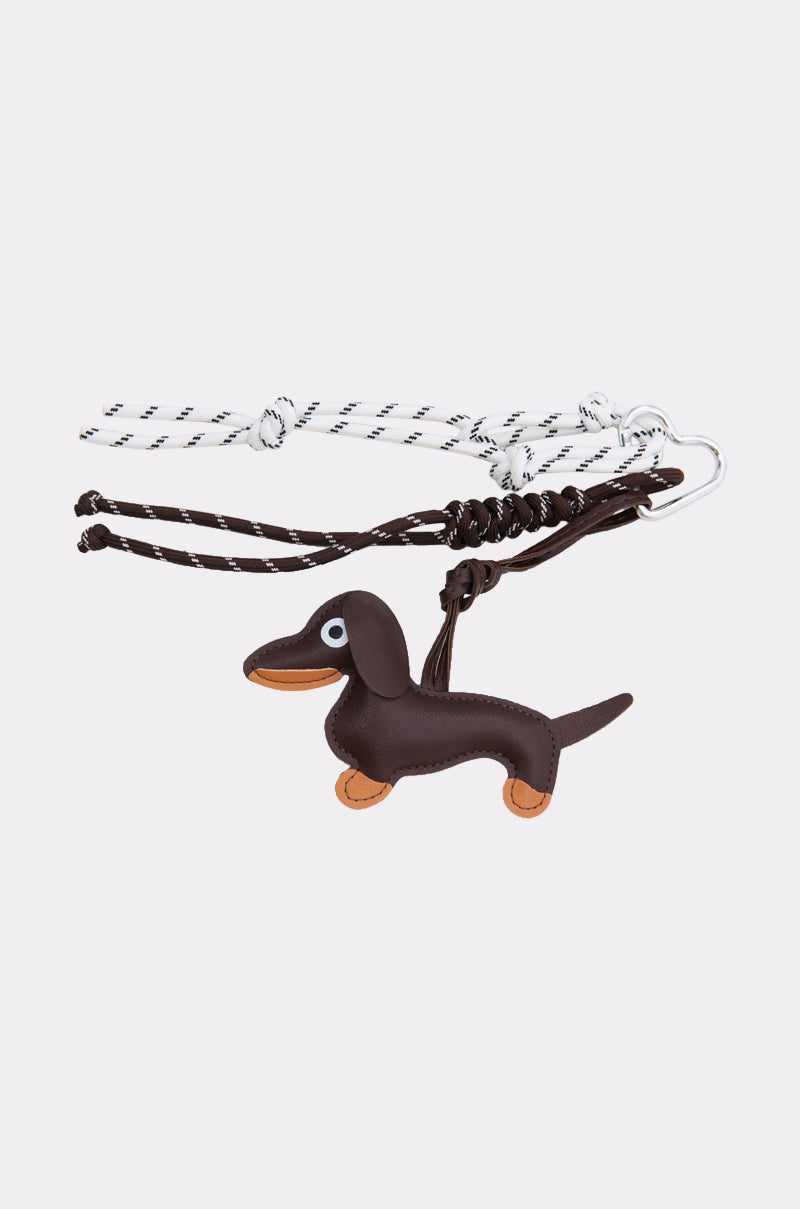 Part of the ULTIMATE KEYCHAIN SET, this keychain features a black and white cord attached to a small brown cartoon-style dachshund charm with tan paws and a smiling face—perfect for fans of bold accessories.