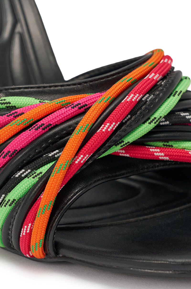 Close-up of the AKIRA GOLD NOWITZKI MULTI WEDGE AND SHOE LACE SANDAL in black faux leather, featuring orange, pink, green, and red patterned braided straps across the front and a sculptural wedge heel. 6