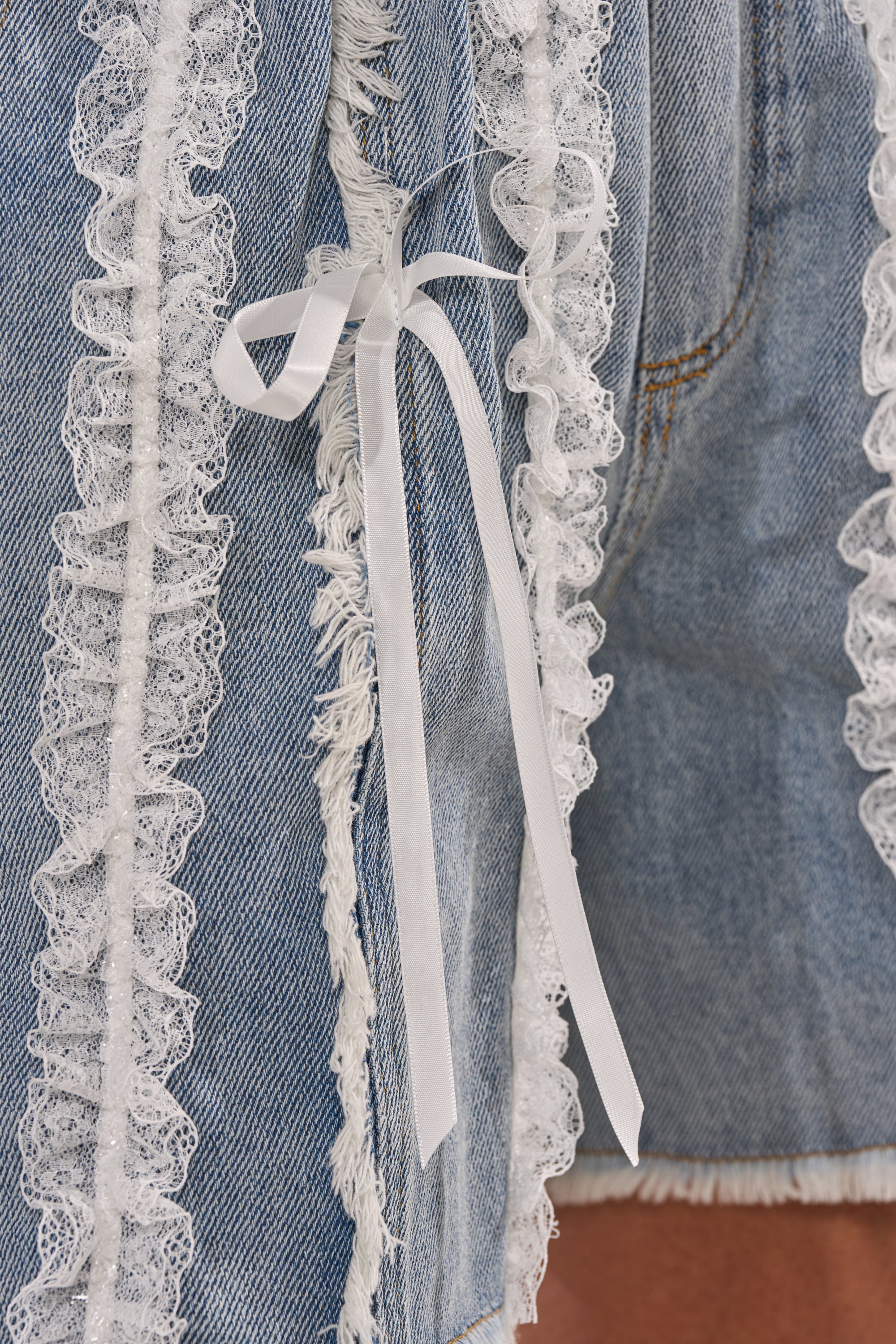 Close-up of TIED AND LACED DENIM SHORTS featuring white lace ruffles, a small white ribbon bow, and rough, frayed hems. 6