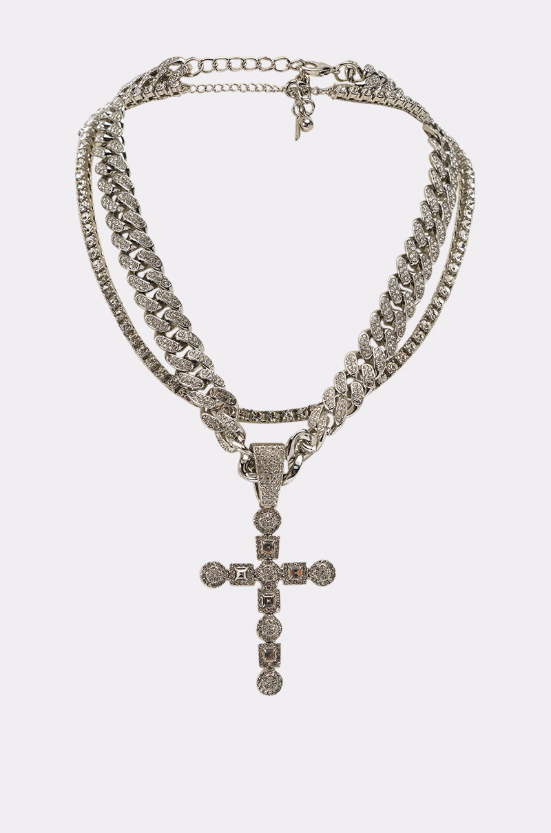 The WHAT U SAY NECKLACE is a layered set with sleek silver chains and a large, ornate rhinestone cross pendant, shown against a plain white background. 0