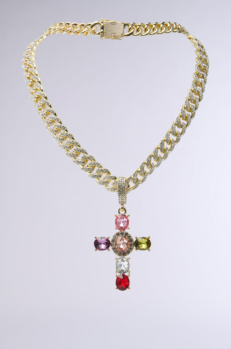 The DOLCE VITA CROSS STATEMENT CHAIN showcases a gold chain necklace with a pendant embellished with multicolored gemstones, featuring pink, green, purple, and red stones. Its chunky chain link design enhances its bold appeal as a statement necklace, exuding elegance and style against a plain white background. 1
