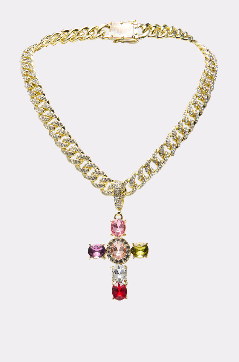 The DOLCE VITA CROSS STATEMENT CHAIN is a chunky gold necklace with a large cross pendant embellished with colorful gemstones—pink, clear, green, purple, red, and black—making a bold statement against a light gray background. 0