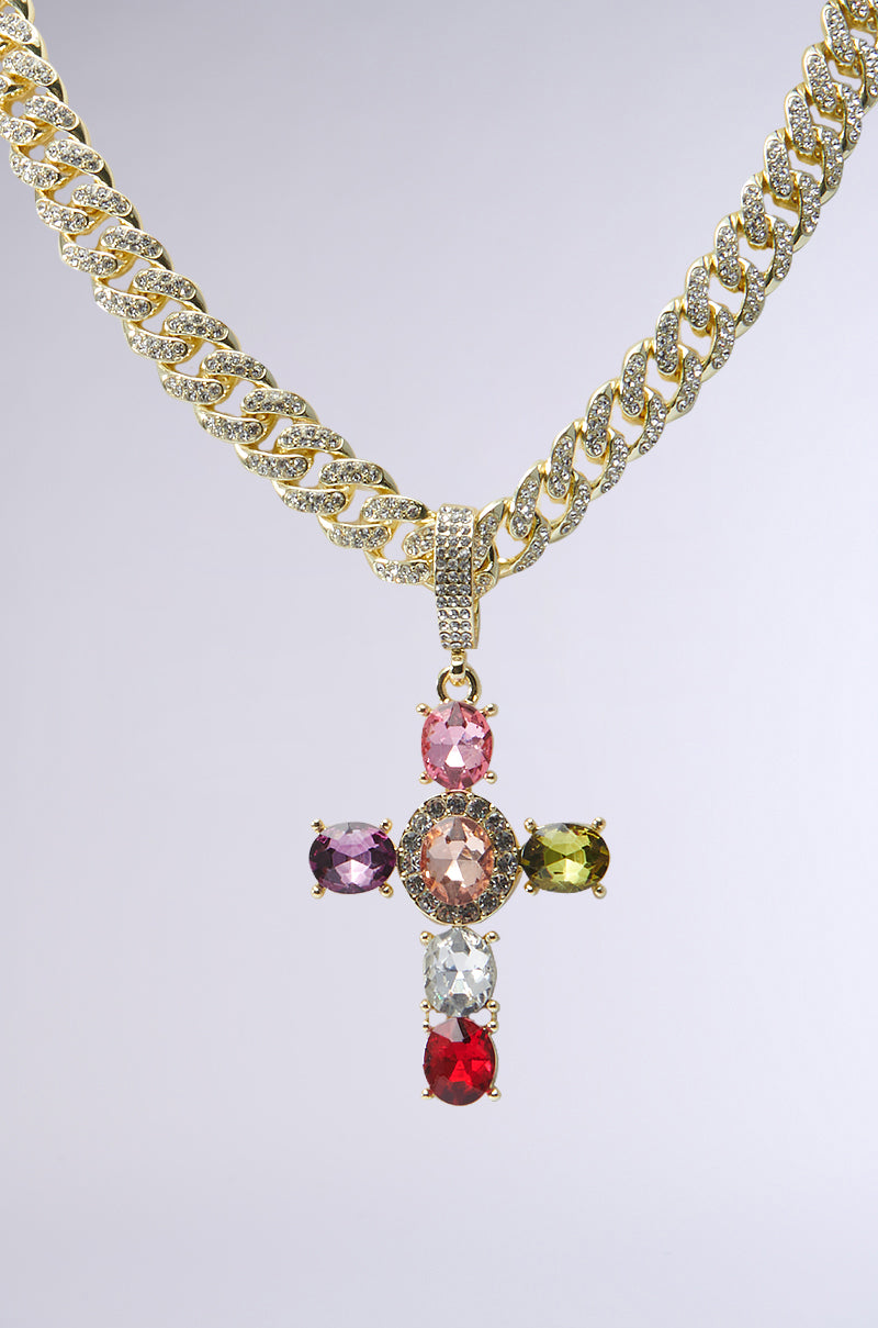 The DOLCE VITA CROSS STATEMENT CHAIN is a chunky chain link necklace with a diamond-encrusted cross pendant embellished with multicolored gemstones in pink, red, green, and clear shades on a light gray backdrop. This statement piece emanates elegance and vibrant style. 4