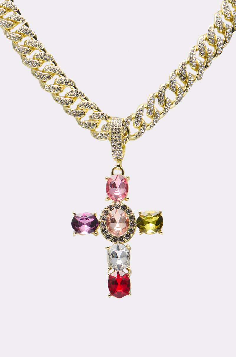The DOLCE VITA CROSS STATEMENT CHAIN is a gold chunky necklace with a bold cross pendant set with five large gemstones—pink, purple, green, red, and clear—and embedded diamonds. 2