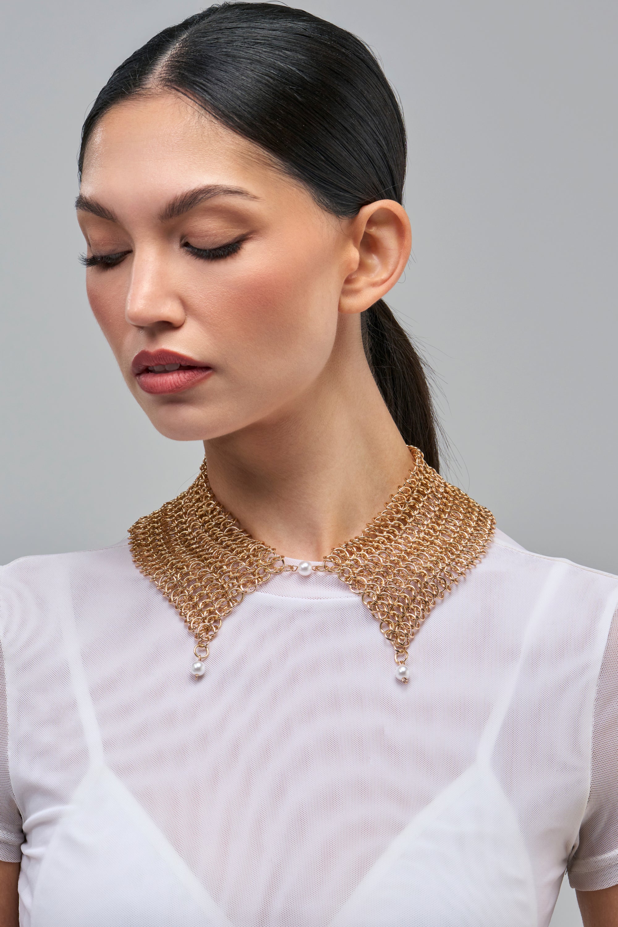 A person wearing a CHAINMAIL PEARL COLLAR, a gold chainmail necklace featuring faux pearl accents at the center and the pointed ends.