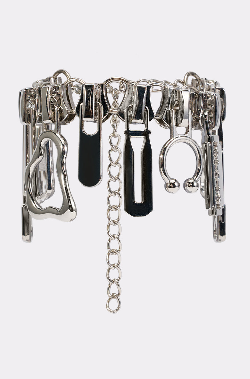 The ZIP IT BRACELET, a silver streetwear accessory featuring an array of metallic zipper pulls, rings, and abstract charms, is displayed against a white background.
