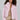 A person with curly hair is dressed in a cozy ensemble, showcasing the BERRIES AND CREAM FAUX FUR JACKET in a fluffy pink hue draped over a sparkly gold dress. They stylishly hold a small handbag while posing against a plain background.