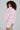 Wearing the BERRIES AND CREAM FAUX FUR JACKET with its oversized lapel collar, a person with curly hair pairs it effortlessly with a patterned skirt, glancing over their shoulder against a plain background.