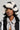 A person wearing a BROOKFIELD FAUX FUR BUCKET HAT, enhancing their outfit with a stylish winter accessory, paired with a snake print shirt and a black-and-white jacket. The background is plain gray.